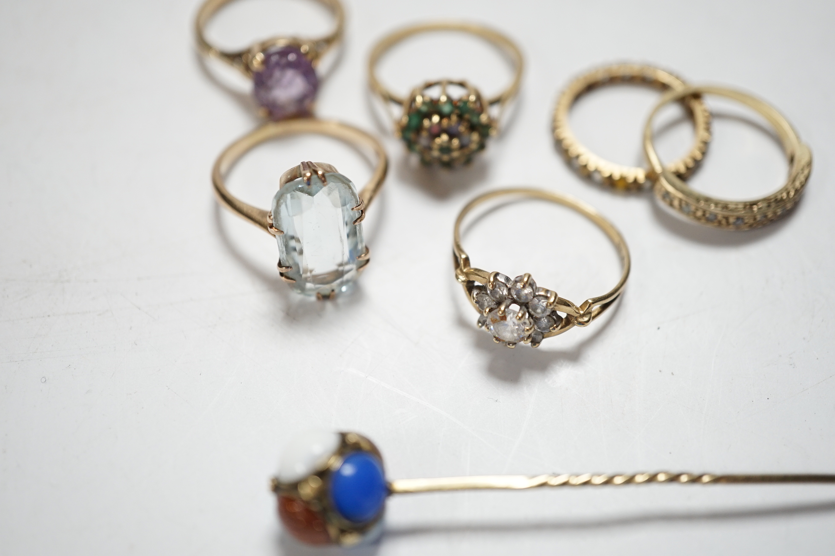 Four assorted modern 9ct and gem set rings including cubic zirconia, two other yellow metal and gem set rings including aquamarine and a yellow metal and multi gem set stick pin, gross weight 15.8 grams.